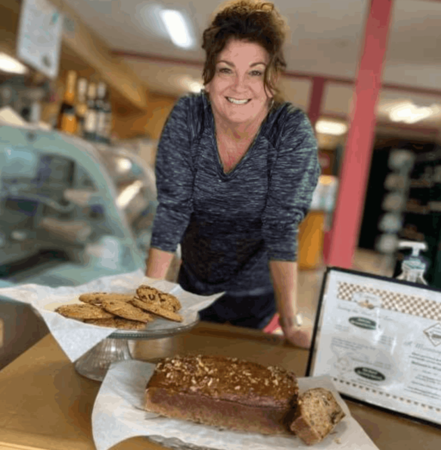 owner kelly harris standing at tablewith baked goods of cookies and breads